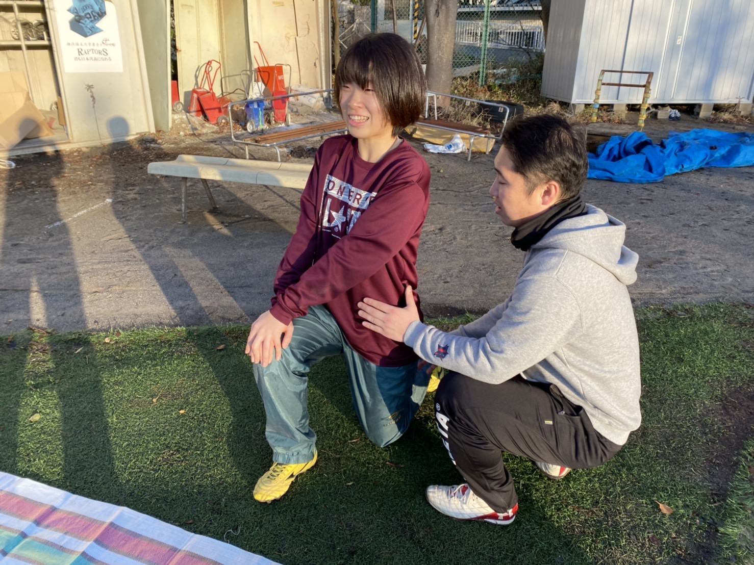 森川稔之が屋外で片膝立ちの女性選手の肩に触れて調整する様子