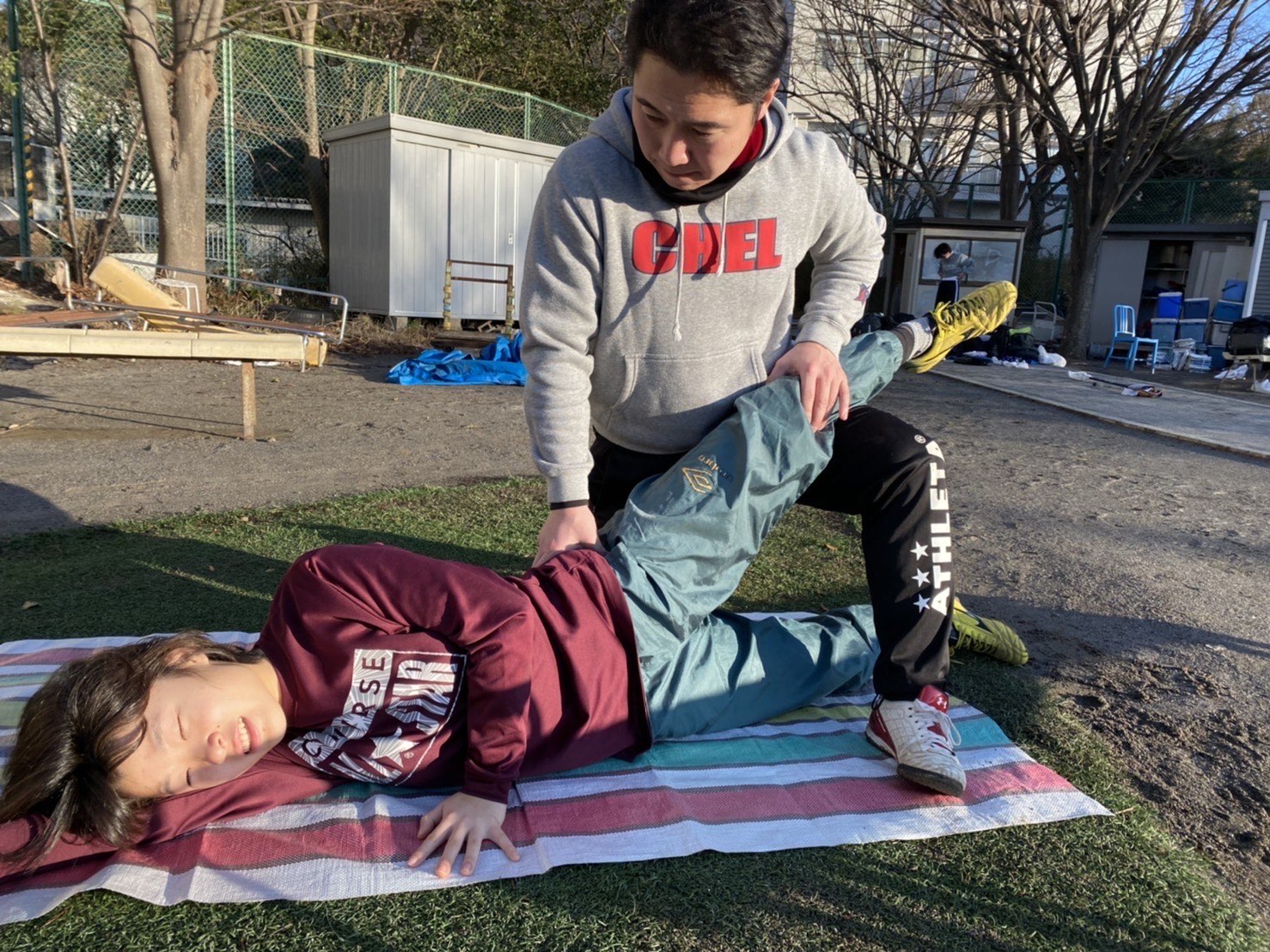森川稔之が屋外で仰向けの選手の脚を持ち股関節の動きを補助する様子