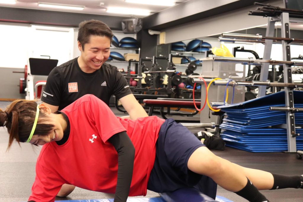 森川稔之がジムで女性選手のサイドプランクを指導する様子
